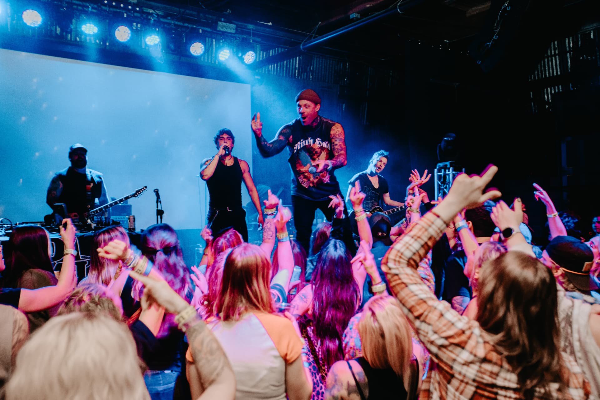 Mccoy performing live on stage with a band, facing a crowd with raised hands under blue stage lights